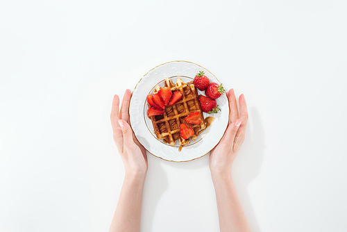 cropped view of woman holding plate with waffle and strawberries on white
