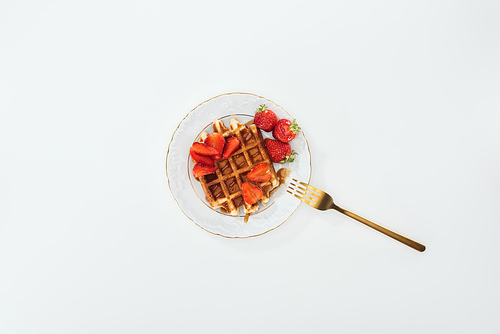 top view of fork on plate with waffle and strawberries on white