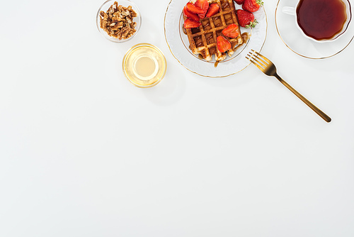 top view of bowls with nuts and honey near tea and plate with waffles on white