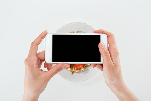 cropped view of woman taking picture of plate with waffle and strawberries isolated on white
