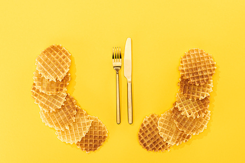 top view of crispy and delicious waffles with cutlery in middle isolated on yellow