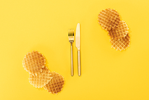 top view of crispy waffles with cutlery in middle isolated on yellow