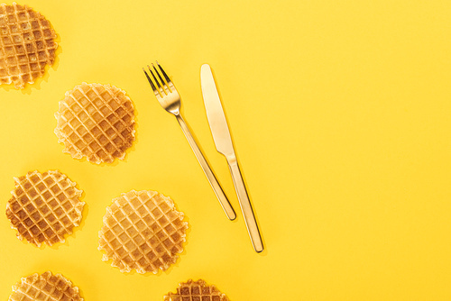 top view of waffles near cutlery in middle isolated on yellow