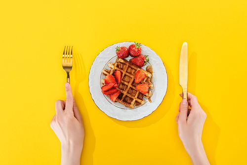 cropped view of woman holding cutlery near waffle on plate on yellow