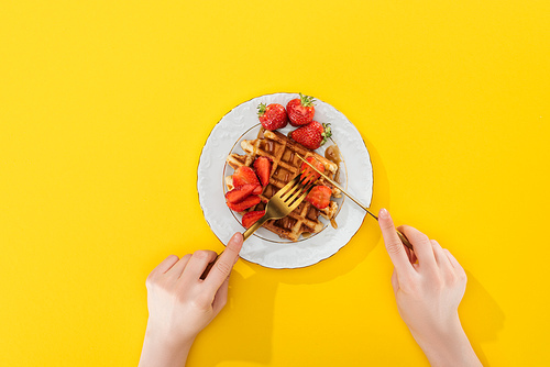 cropped view of woman cutting waffle on plate on yellow