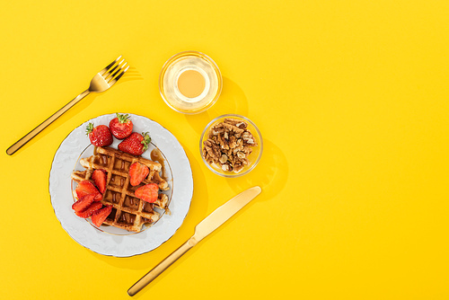 top view of served breakfast with waffles, berries, honey and nuts near cutlery on yellow