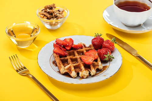 served breakfast with waffle, strawberries, honey, nuts and tea on yellow