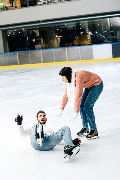 worried couple spending time on skating rink while man falling on rink