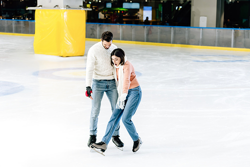 young couple skating together while woman falling on rink