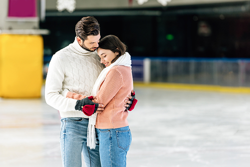 young couple in sweaters hugging on skating rink