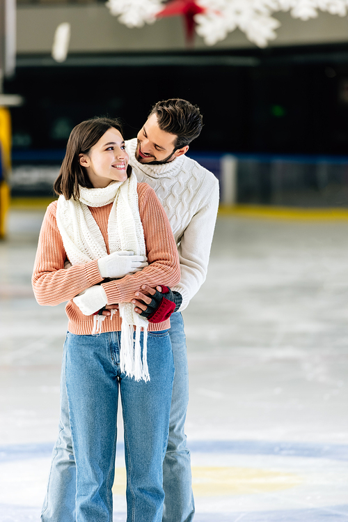 happy young couple in sweaters hugging on skating rink