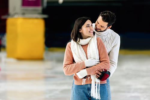 young positive couple in sweaters hugging on skating rink