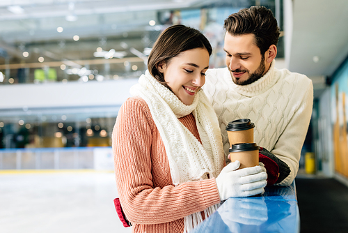 beautiful happy couple holding coffee to go on skating rink