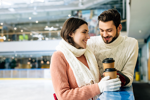 smiling couple holding coffee to go on skating rink