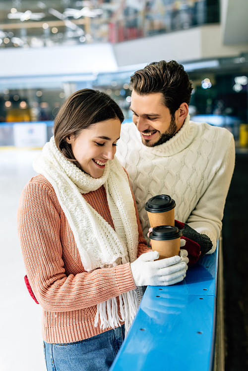 beautiful positive couple holding coffee to go on skating rink