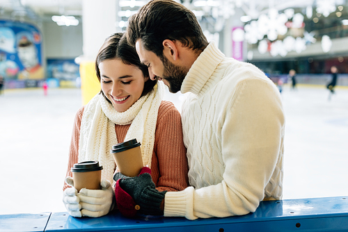 beautiful happy couple smiling and holding coffee to go on skating rink