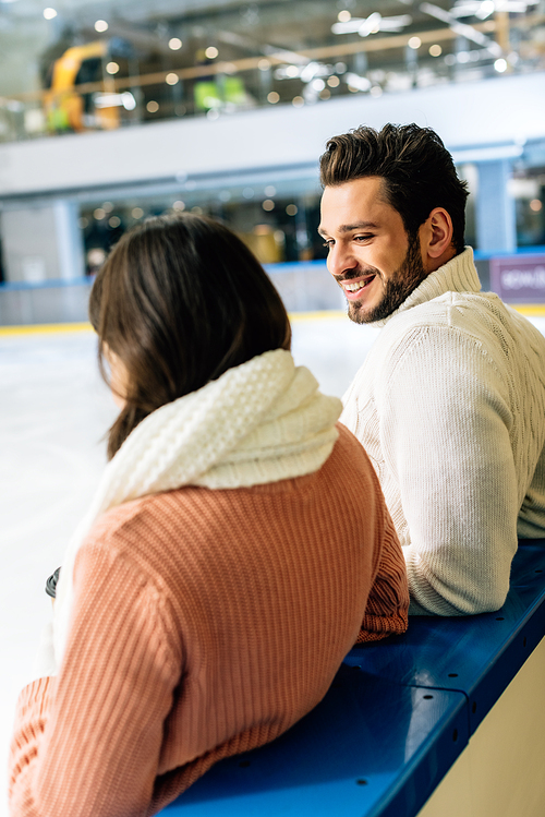 cheerful couple in sweaters spending time on skating rink