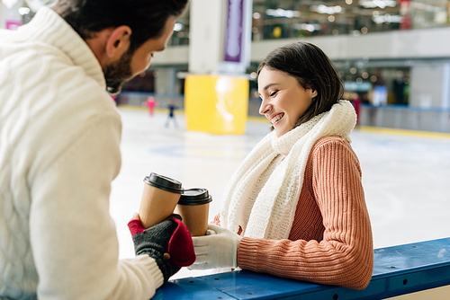 beautiful girlfriend and happy boyfriend holding coffee to go on skating rink