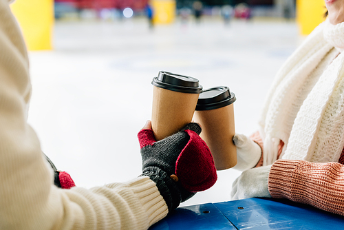 cropped view of couple holding paper cups of coffee to go on skating rink