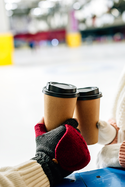 cropped view of couple holding disposable cups of coffee to go on skating rink