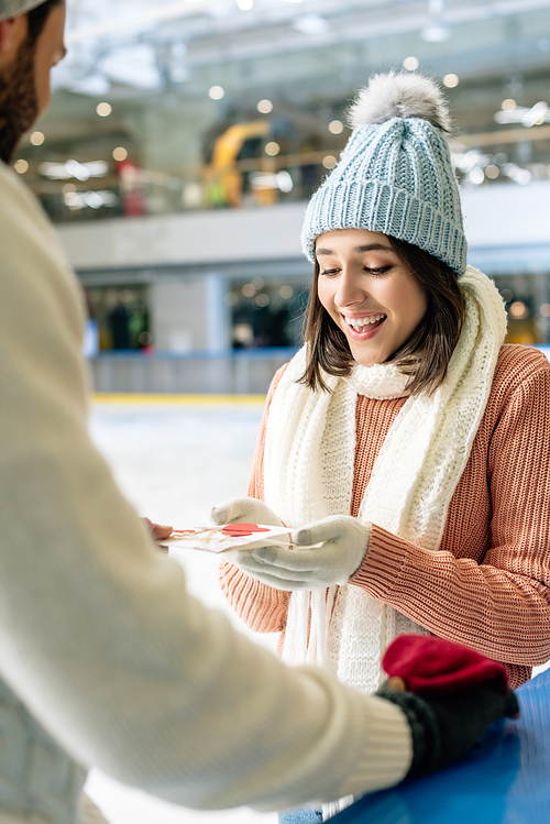 man giving greeting card on valentines day to happy woman on skating rink