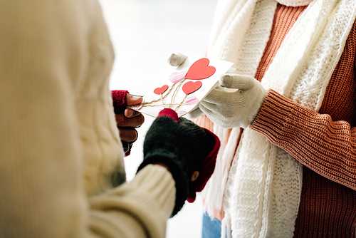 cropped view of man giving greeting card with hearts on valentines day to woman on skating rink