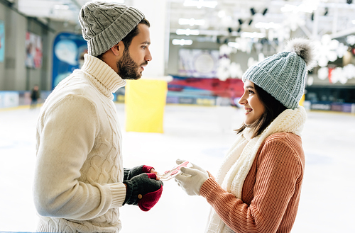 handsome man giving greeting card on valentines day to cheerful woman on skating rink