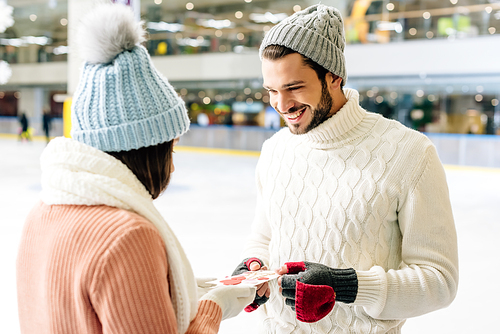 smiling man giving greeting card on valentines day to woman on skating rink