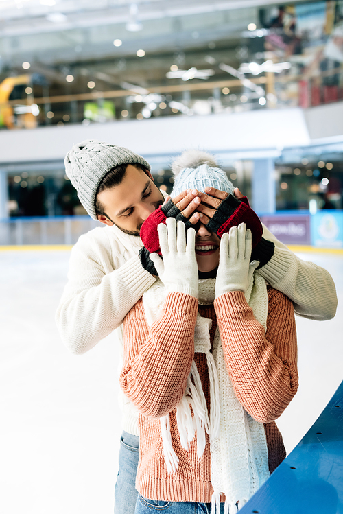 cheerful man closing eyes to woman to make a surprise on skating rink