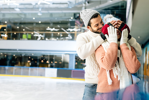 handsome boyfriend closing eyes to girlfriend to make a surprise on skating rink