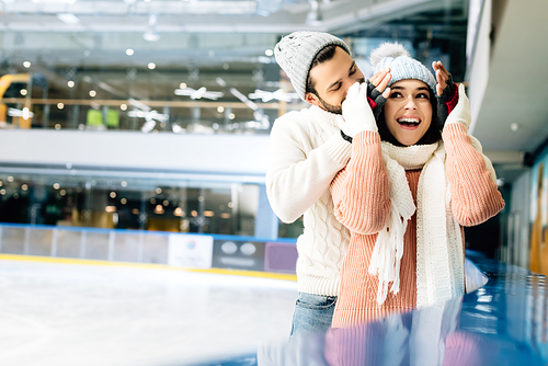 cheerful man closing eyes to excited woman to make a surprise on skating rink