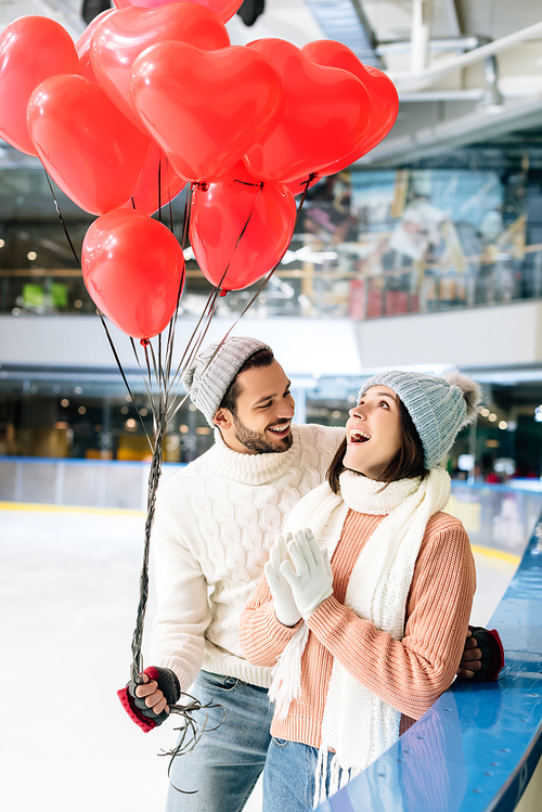 excited couple in winter outfit with red heart shaped balloons spending time on skating rink on valentines day