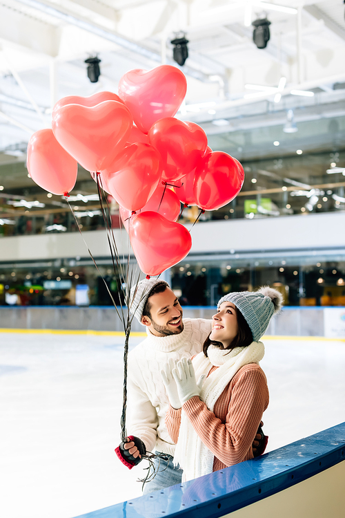 beautiful couple with red heart shaped balloons spending time on skating rink on valentines day