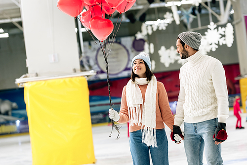 cheerful couple with red heart shaped balloons spending time on skating rink on valentines day