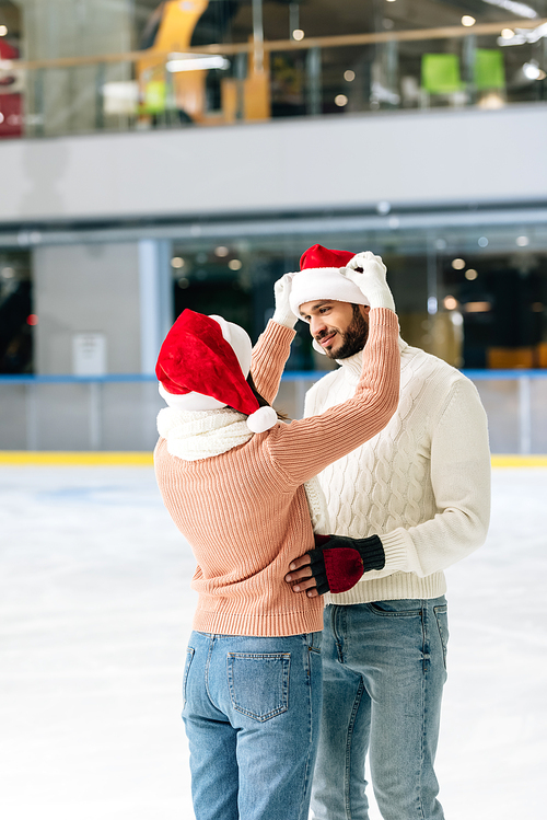 beautiful happy couple in santa hats spending time on skating rink