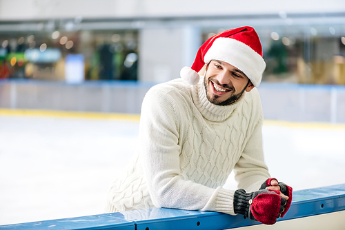 happy man in sweater and santa hat on skating rink