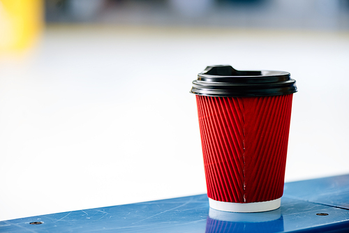 red disposable cup of coffee to go standing on railing of skating rink