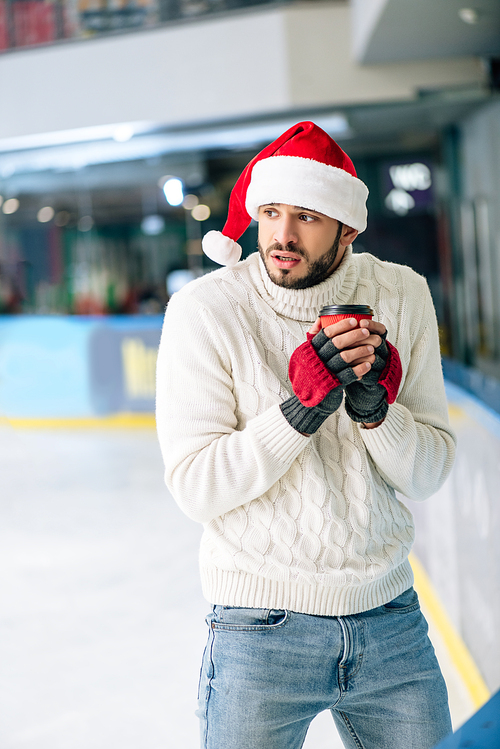 cold man in sweater and santa hat holding coffee to go on skating rink