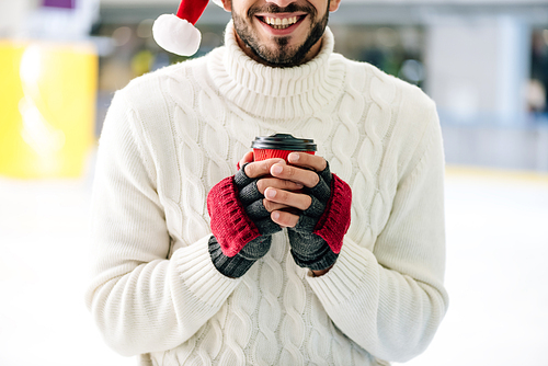 cropped view of cheerful man in santa hat holding coffee to go on skating rink