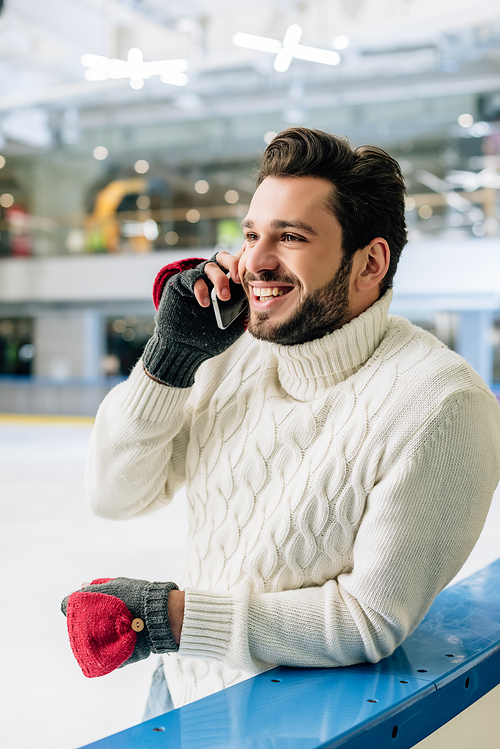 cheerful man in sweater talking on smartphone on skating rink