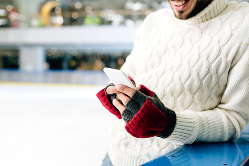 cropped view of man in sweater using smartphone on skating rink