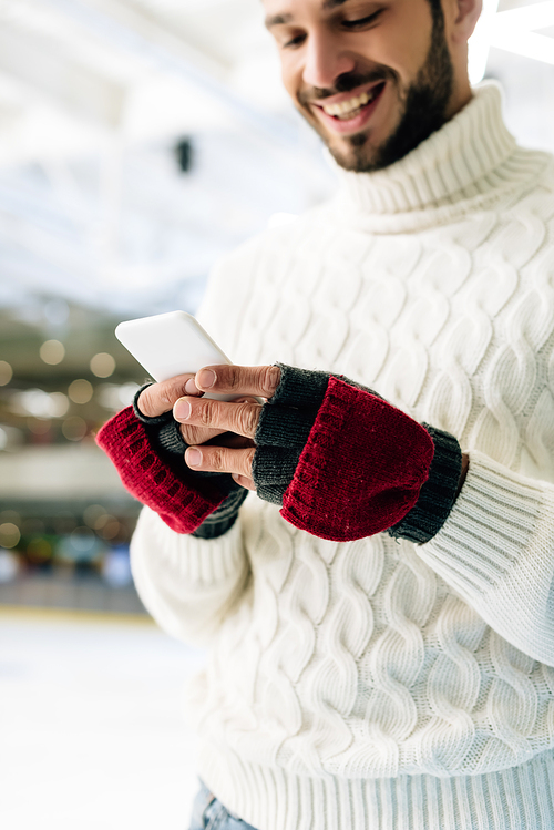 cheerful man in sweater using smartphone on skating rink