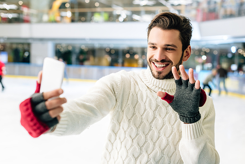 cheerful man waving hand and using smartphone on skating rink