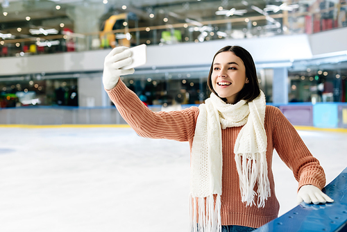 cheerful girl taking selfie on smartphone on skating rink