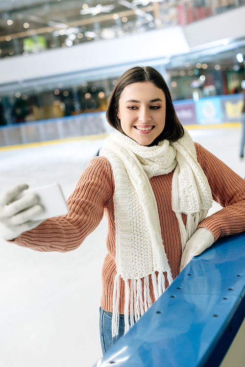 beautiful smiling girl taking selfie on smartphone on skating rink