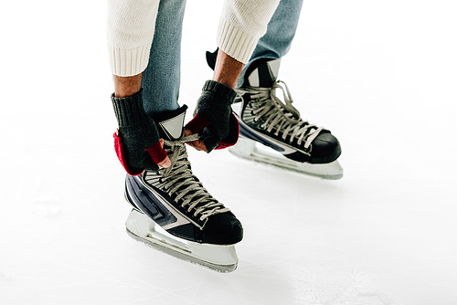 cropped view of man tying shoelaces of skates on skating rink