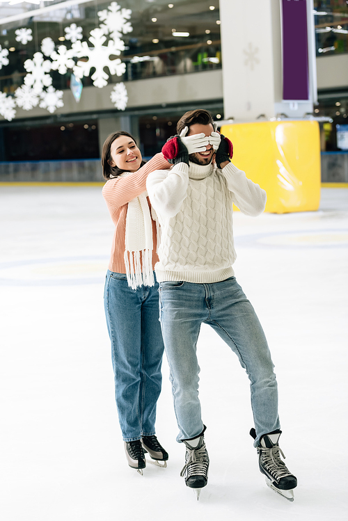 cheerful woman closing eyes to man to make a surprise on skating rink