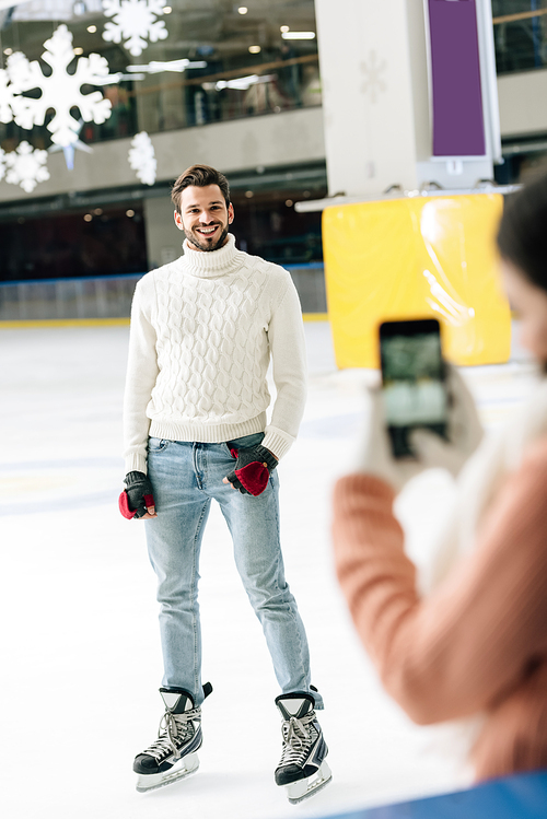 selective focus of woman taking photo of handsome smiling man on smartphone on skating rink