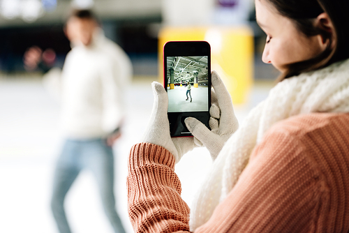 selective focus of beautiful woman taking photo of man on smartphone on skating rink