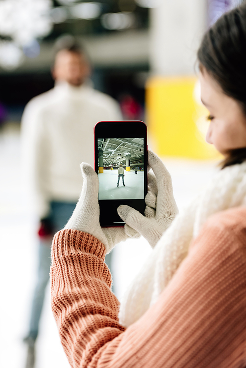 selective focus of woman taking photo of man on smartphone on skating rink